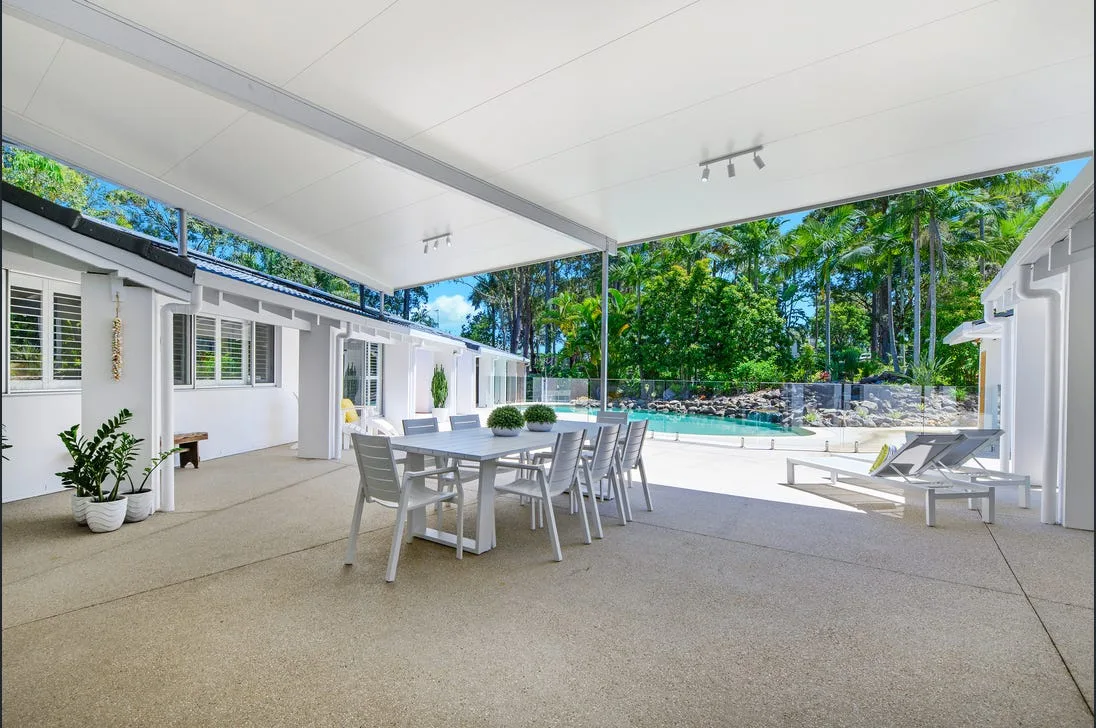 Covered concrete patio with outdoor dining setting beside a pool