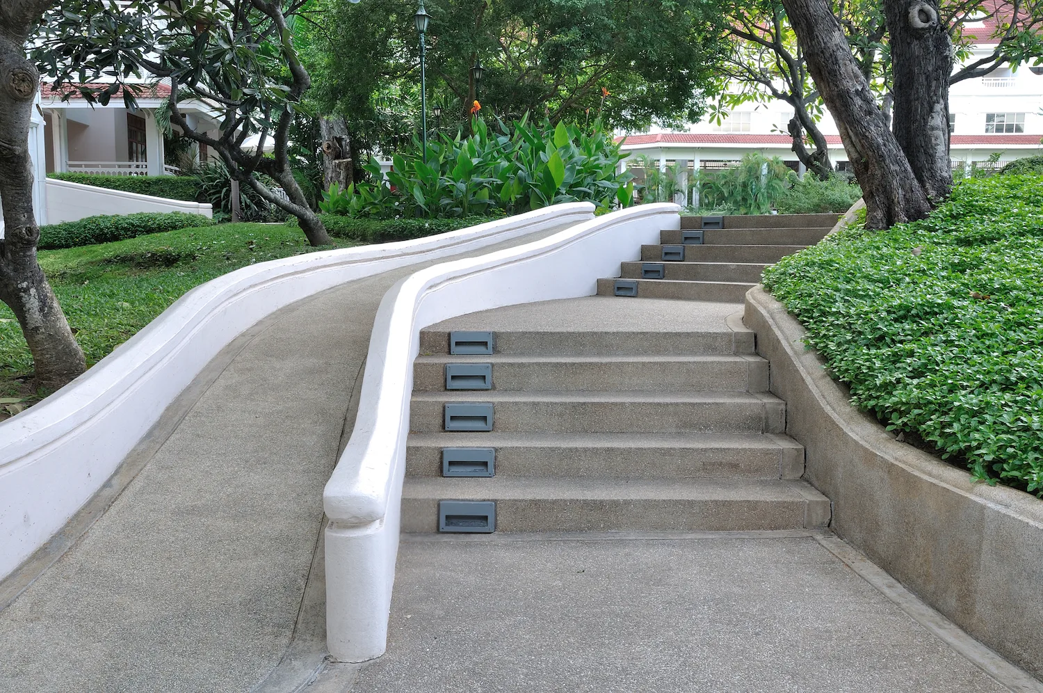 Concrete stairs and ramp with a curved handrail through a garden
