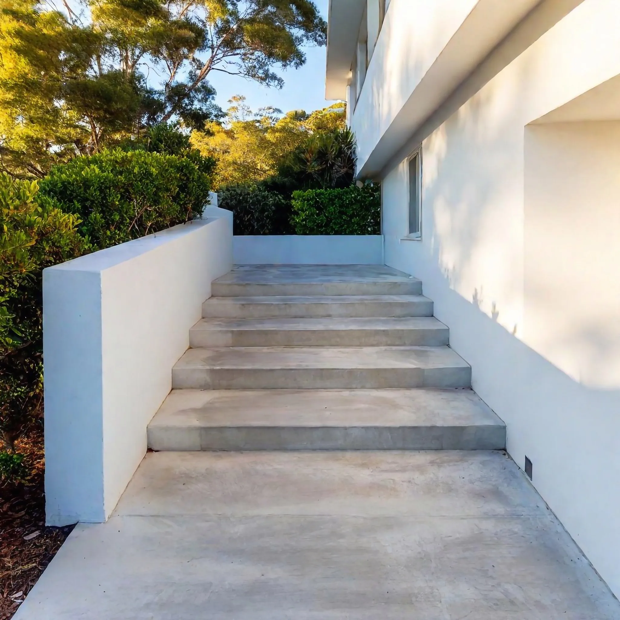 Concrete stairs rising between rendered walls to a home entrance